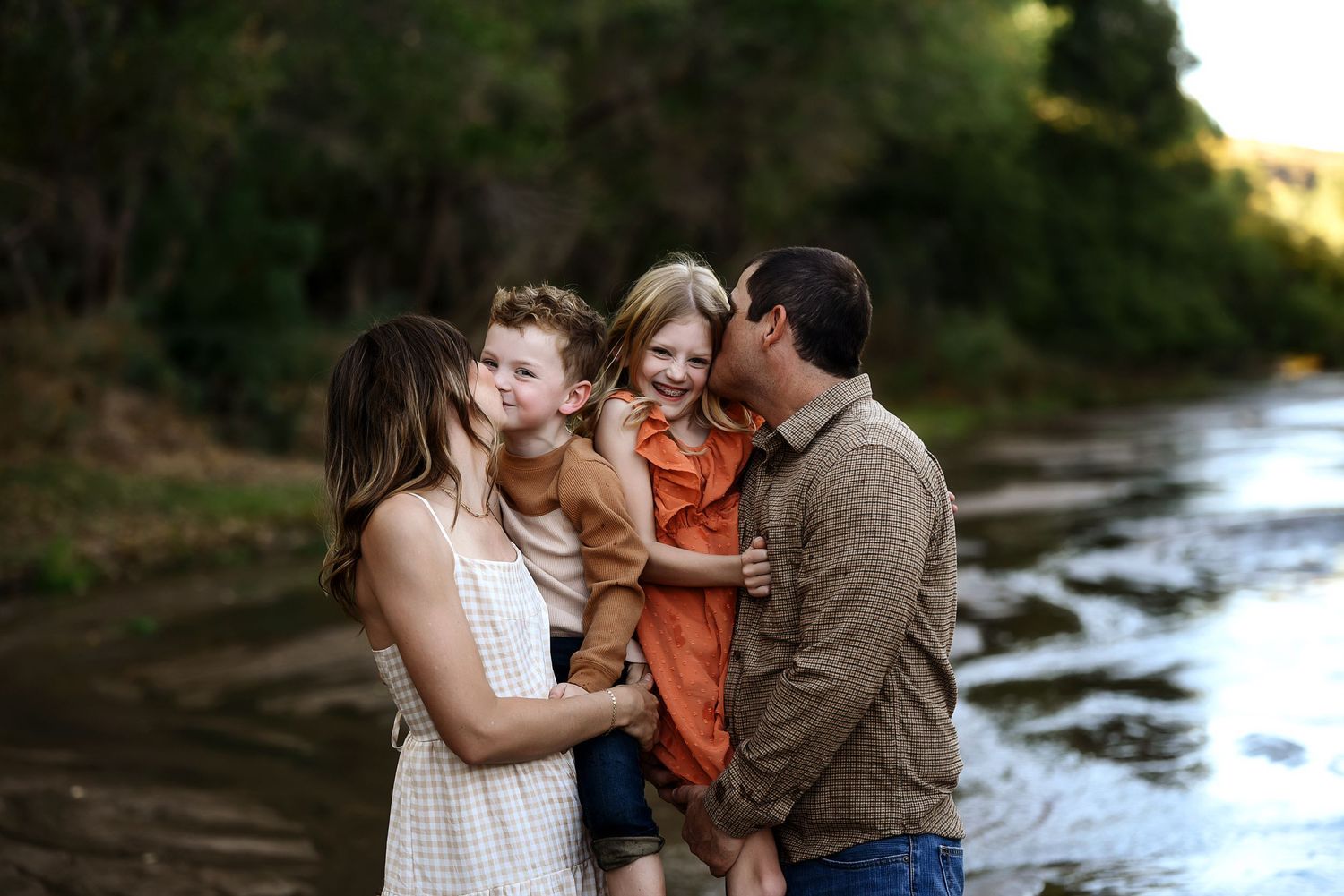 Happy family of four laughing together by a scenic river outdoors.
