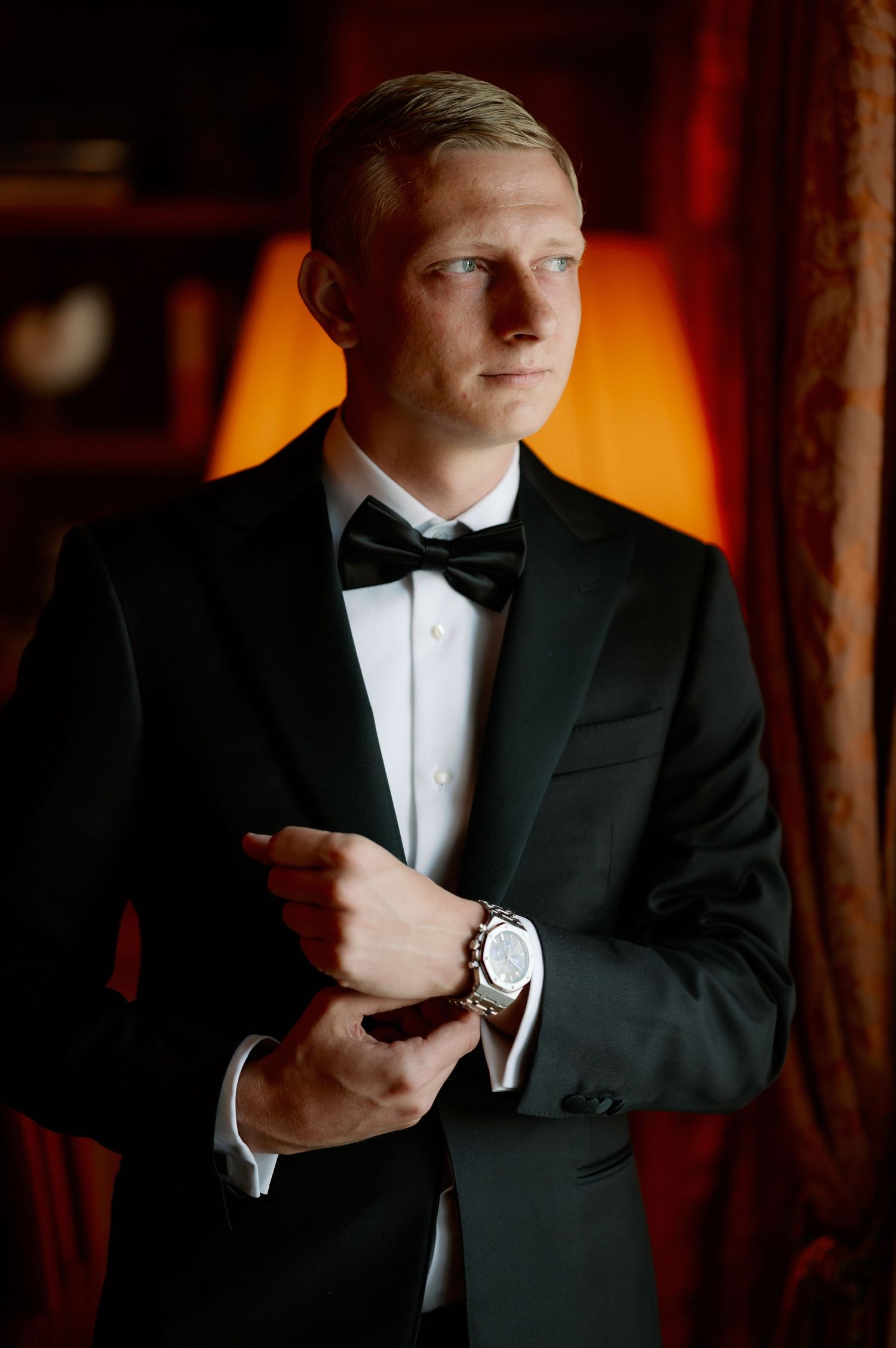 An elegant portrait with warm lighting showing a tuxedo and luxury watch.