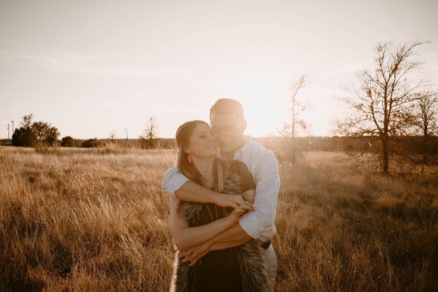 Silhouetted couple embracing in warm sunset light amidst prairie landscape.