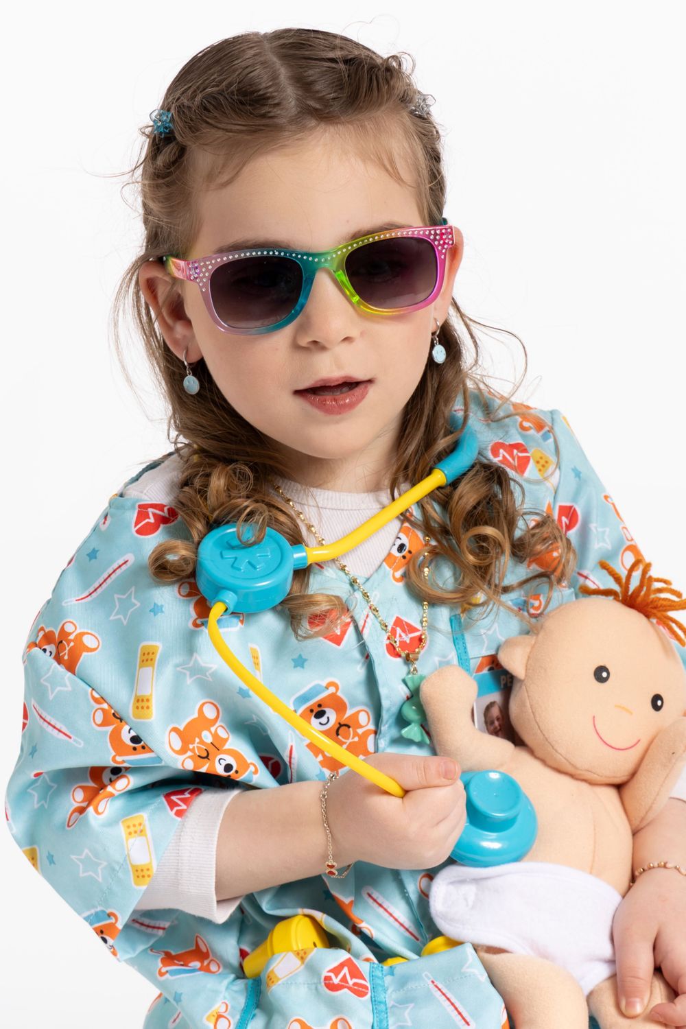 Young child wearing colorful sunglasses and fox print pajamas while holding baby doll.
