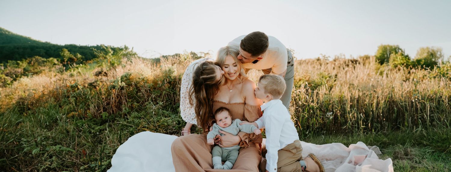 A family shares an intimate moment together on a picnic blanket in a sunlit meadow.