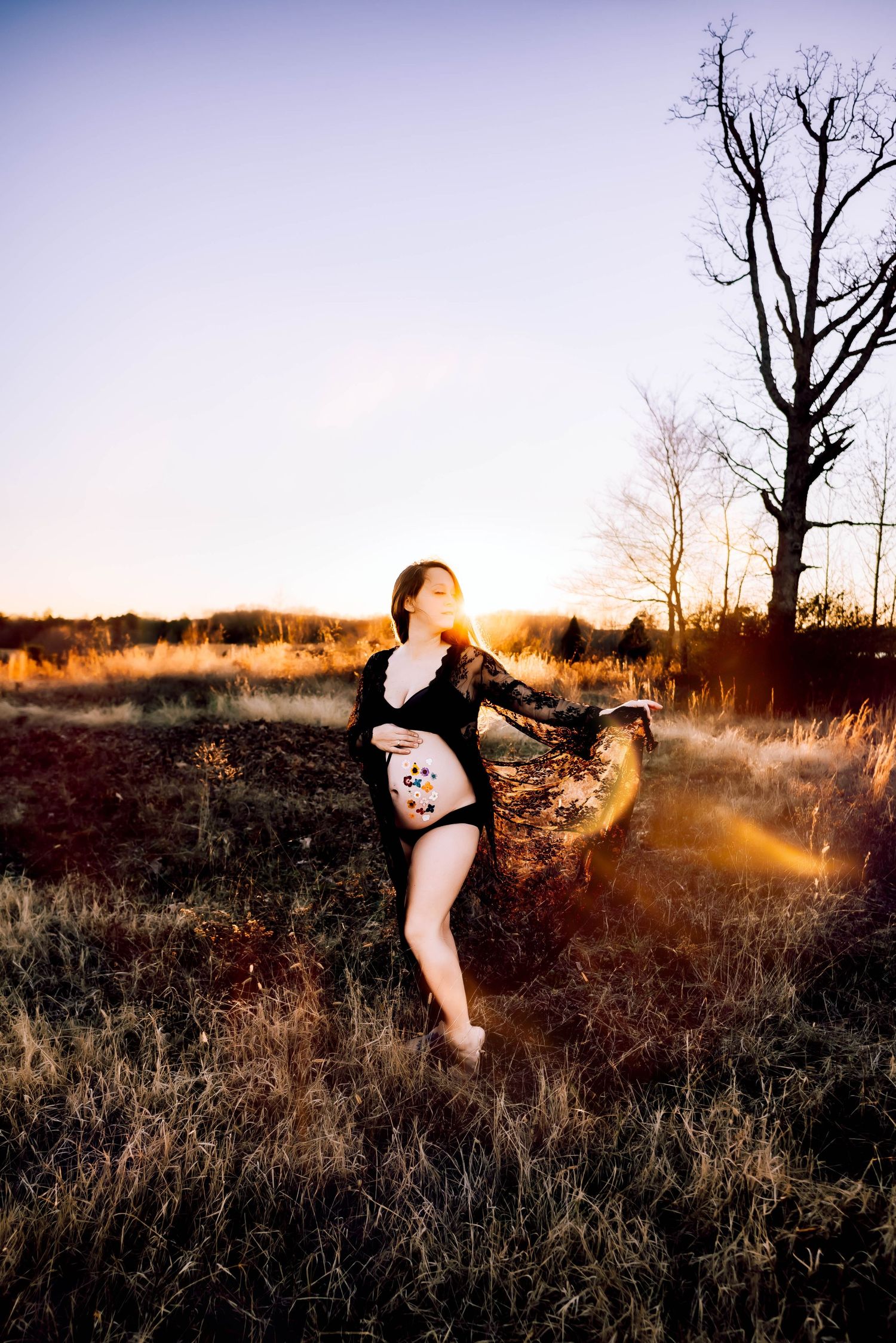 Dreamy sunset portrait with lens flare in a field with bare trees.