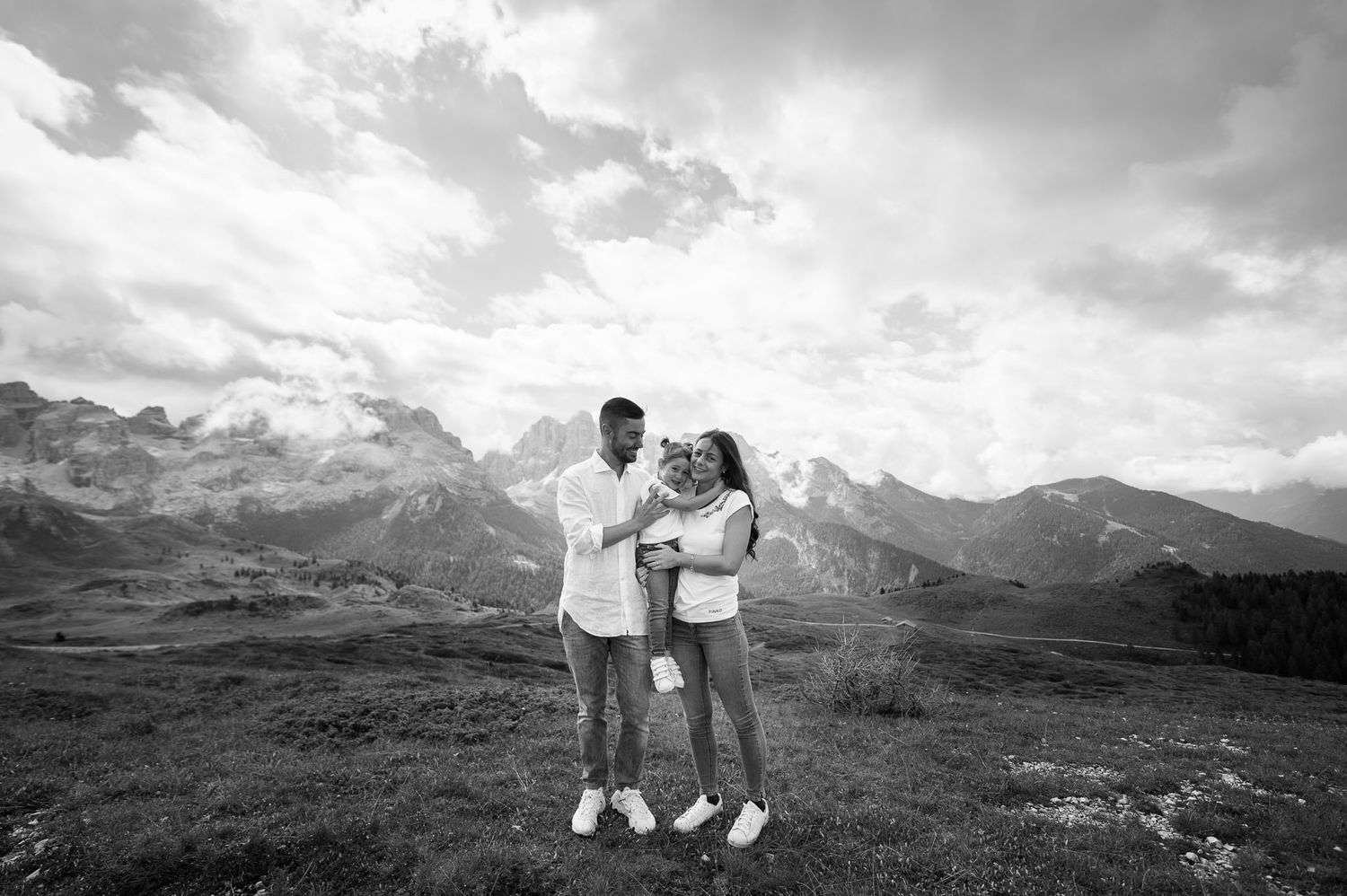 Black and white photo of couple standing together against dramatic mountain landscape.