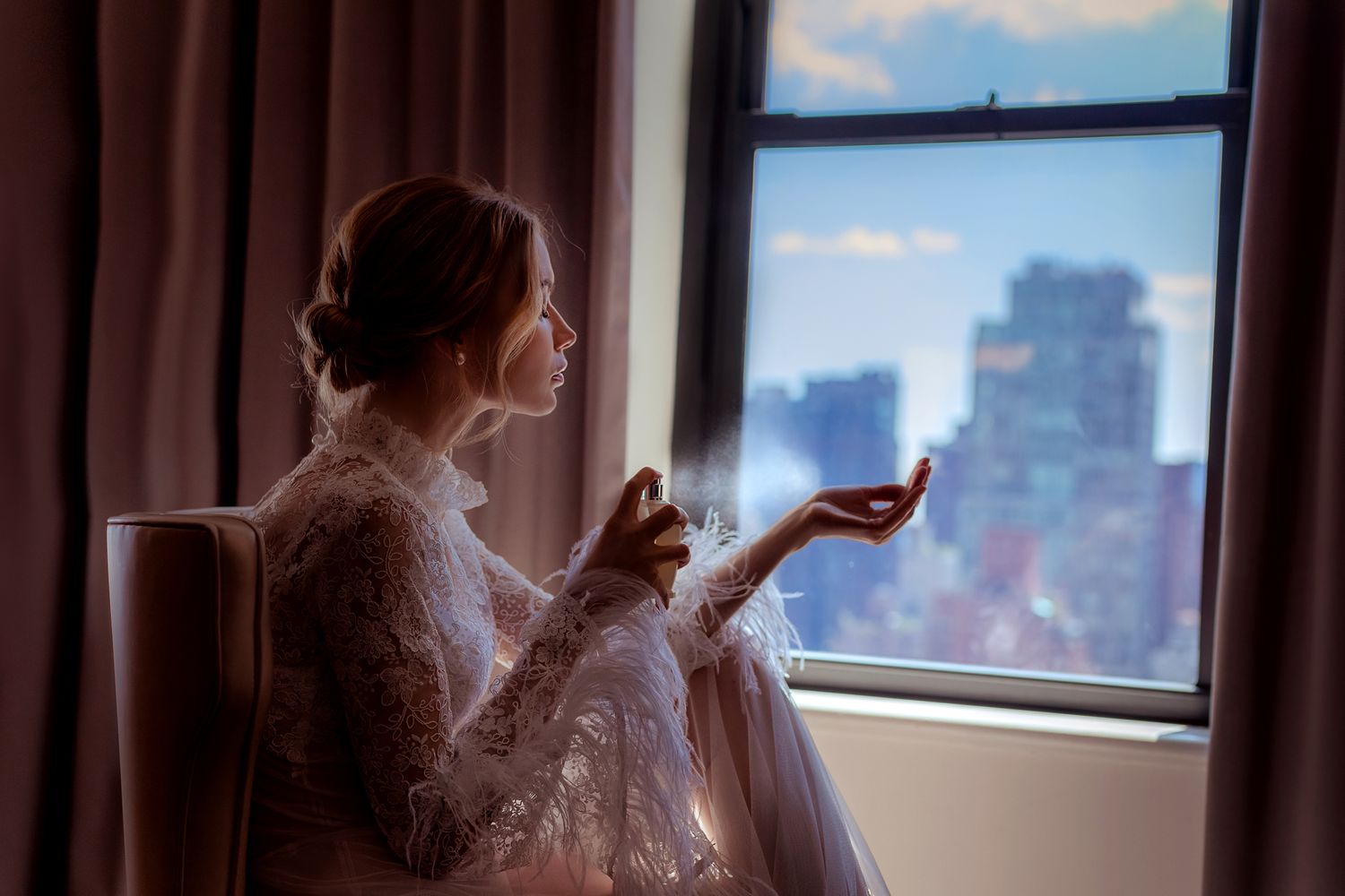 Silhouette of person in lace dress gazing out city window at sunrise.