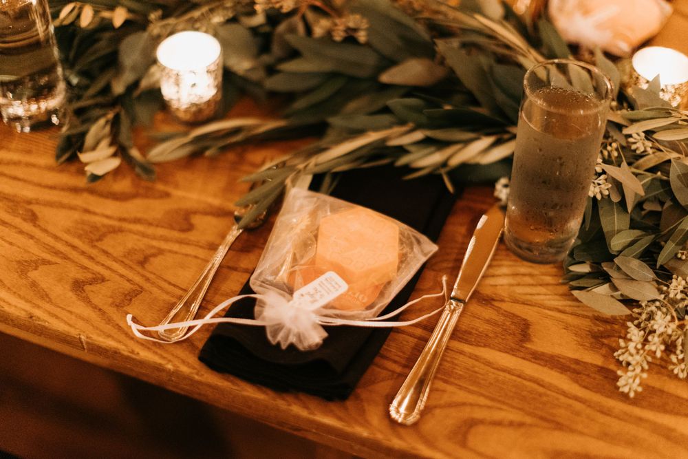 Elegant fall wedding place setting with wrapped favor, black napkin, and greenery table runner with candles.