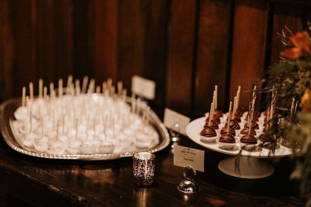 Elegant dessert table displays rows of cake pops and chocolate treats at a wedding.