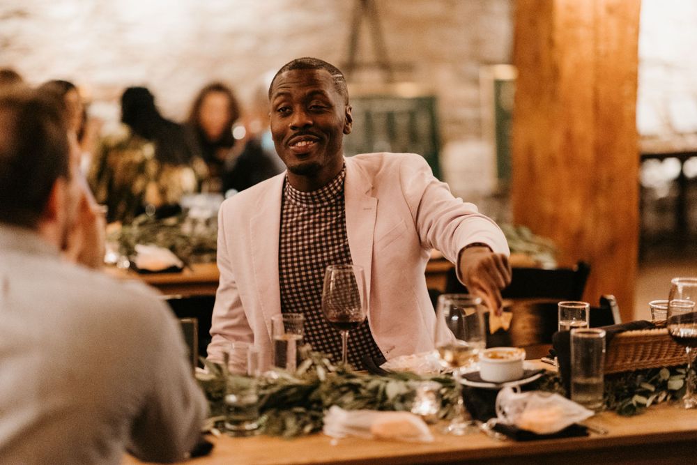 Smiling guest in pink blazer enjoying wedding reception dinner at rustic stone venue.