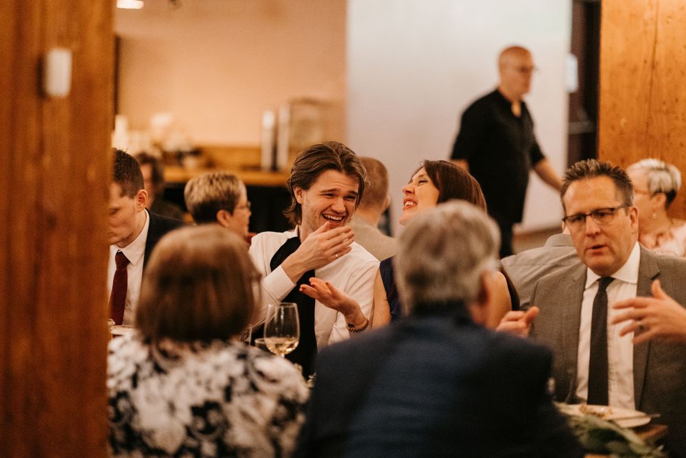 Wedding guests laughing and enjoying conversation at elegant rustic reception dinner tables.