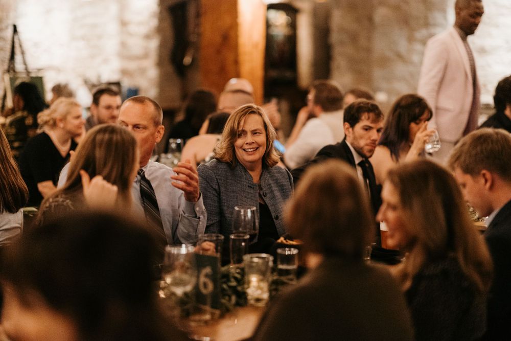 Wedding guest smiles warmly while seated at a candlelit reception table in a rustic stone venue.