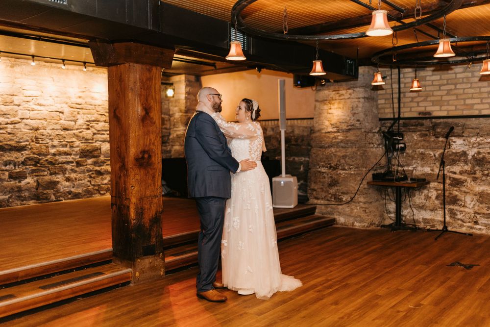 Bride and groom sharing a tender first dance in a warmly lit rustic stone-walled venue.