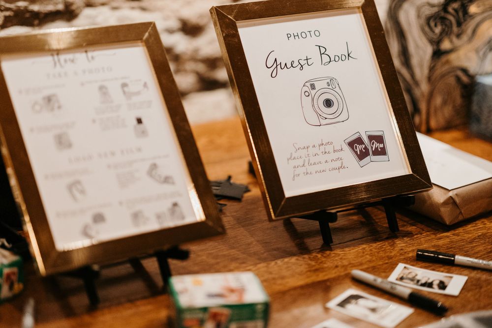 Wedding photo guest book display with Instax camera sign and polaroid photos on wooden table.