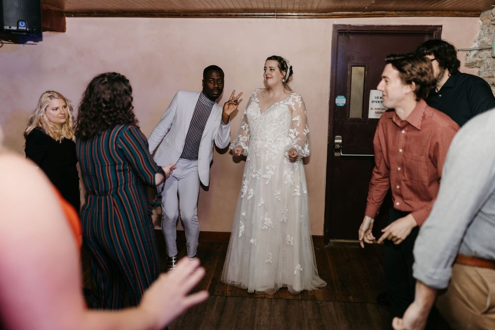 Bride in lace gown dances and celebrates with guests including groom in white suit.