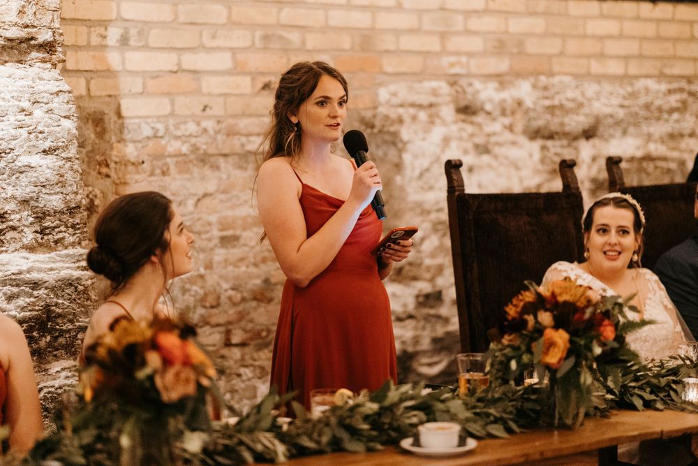 Bridesmaid in burgundy dress gives a toast holding a microphone at an elegant wedding reception.