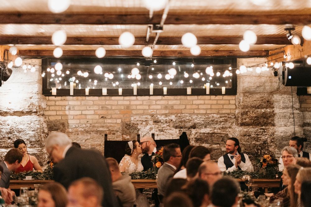Romantic wedding reception in a rustic stone venue with Edison bulb string lights overhead.