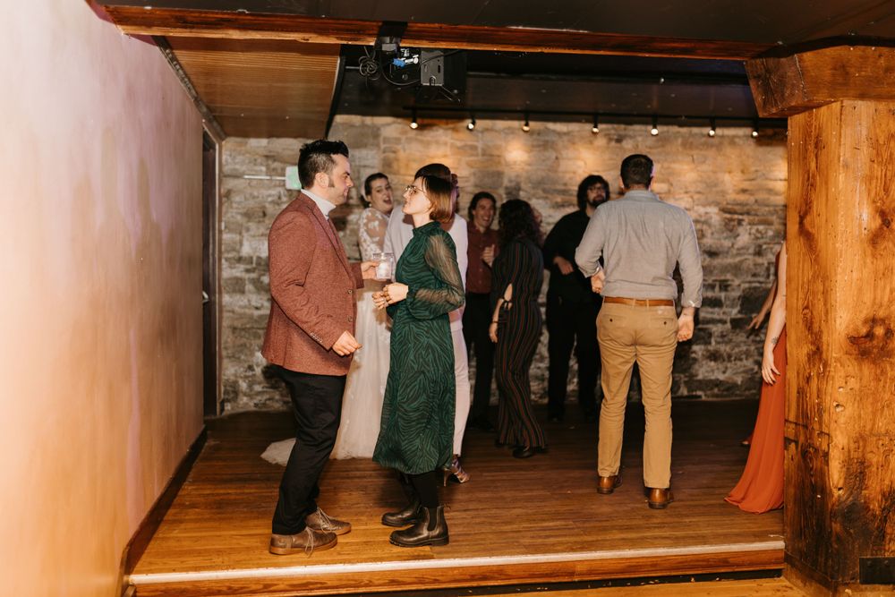 Wedding guests mingle and dance in a rustic stone-walled venue during the reception.