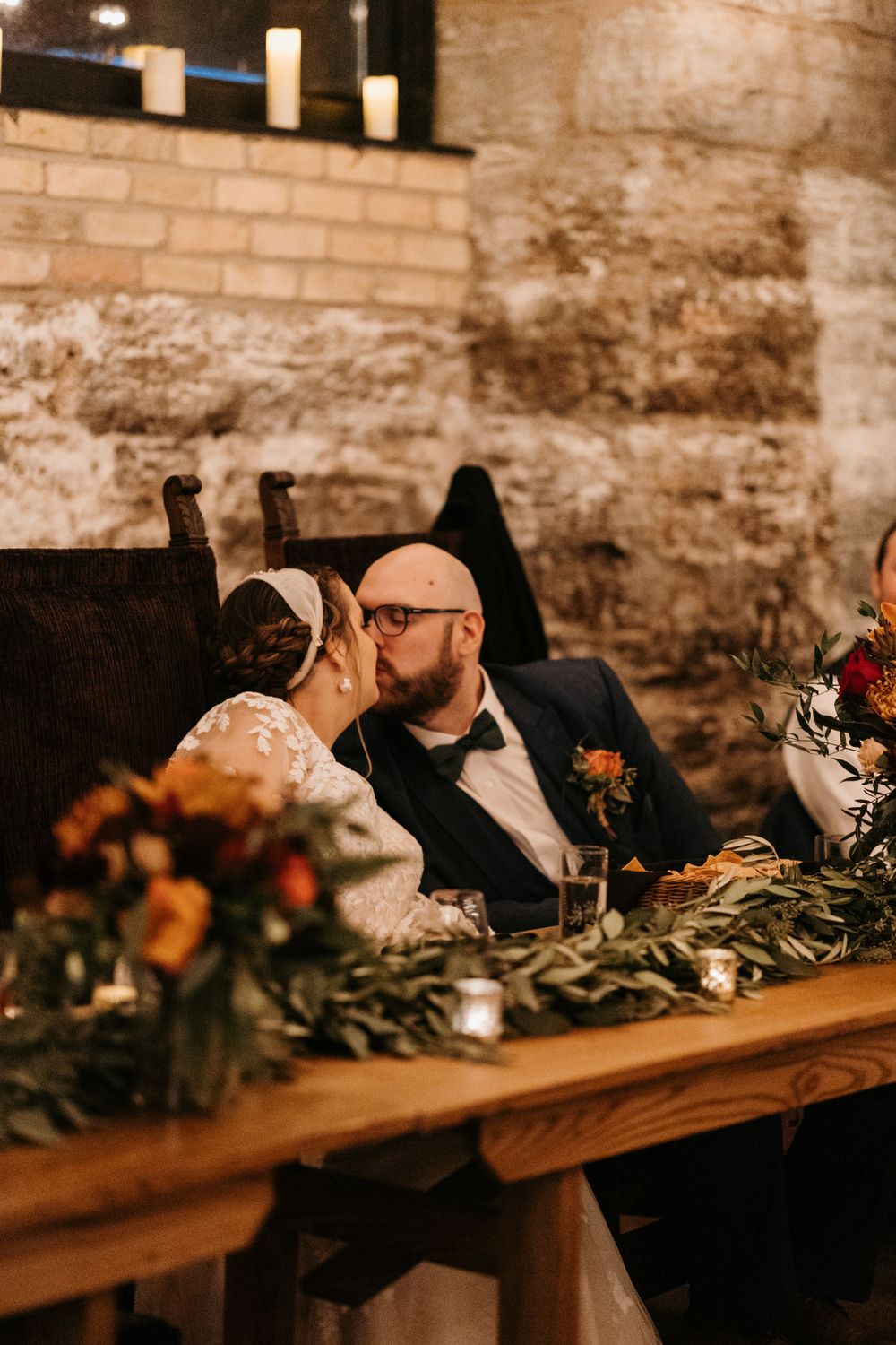 Bride and groom share a kiss at their sweetheart table decorated with autumn floral arrangements.