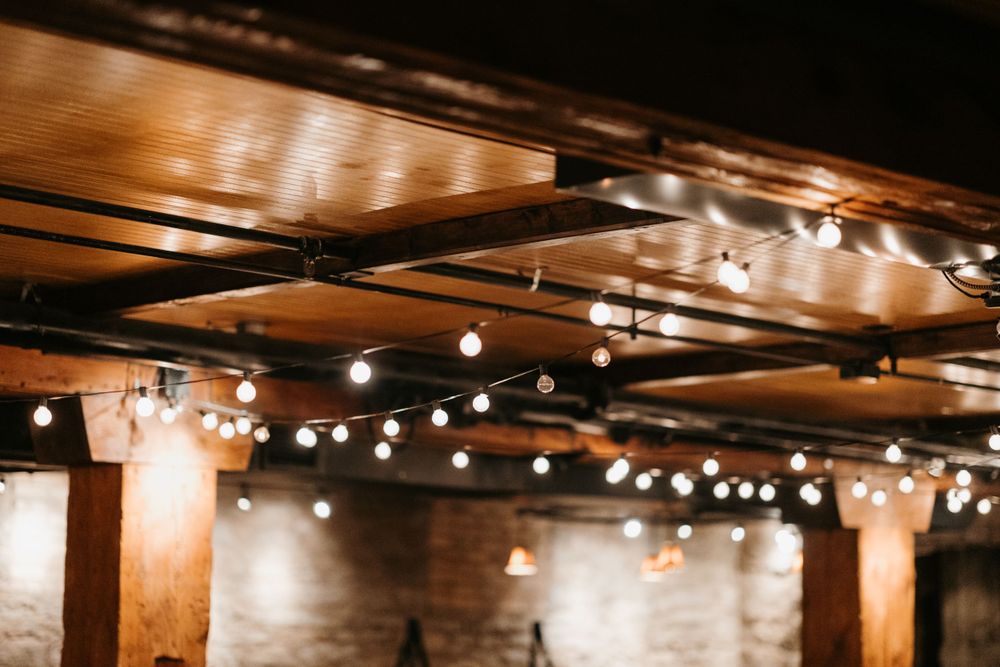 Warm Edison string lights hanging from rustic wooden ceiling beams in wedding reception venue.
