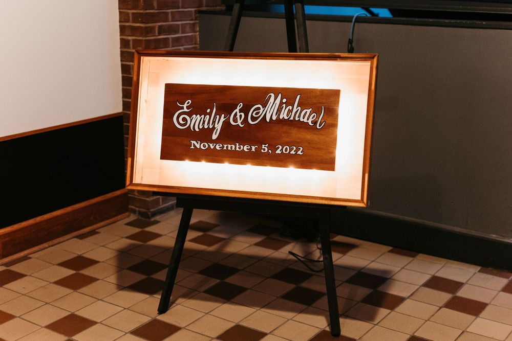 Illuminated wooden wedding sign reading Emily and Michael November 5 2022 displayed on black easel.