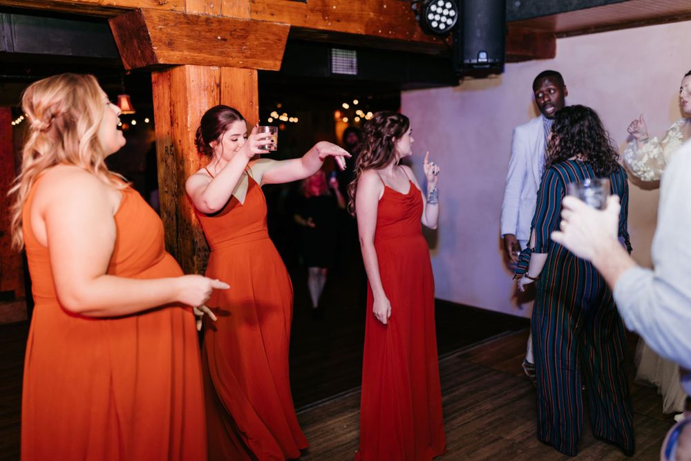 Bridesmaids in rust-colored dresses dance joyfully with guests at a wedding reception.