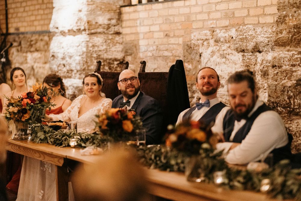 Wedding party smiles at the head table adorned with lush autumn floral arrangements at reception.