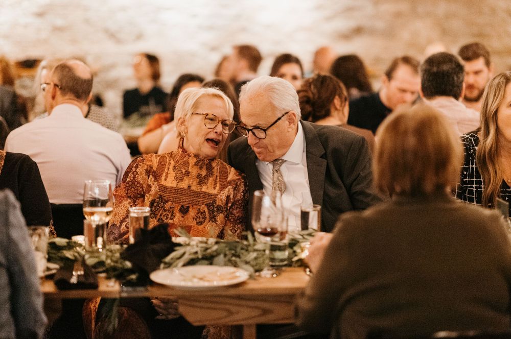 Elderly couple sharing an intimate moment at a warmly lit rustic wedding reception dinner.