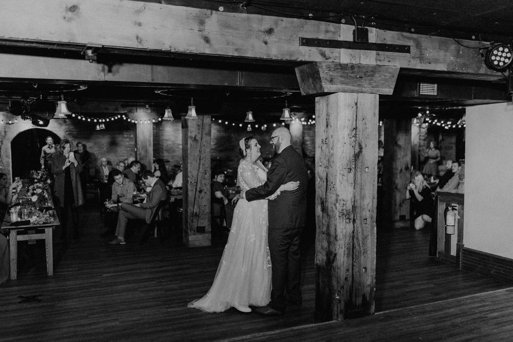 Bride and groom sharing their first dance in a rustic venue, black and white photo.