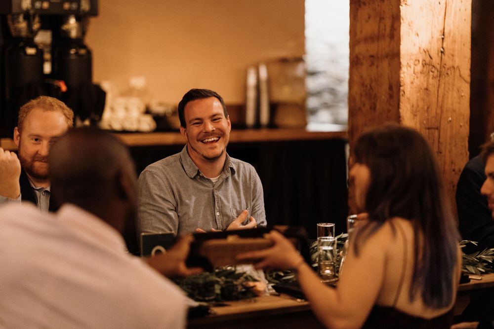 Guest smiling and laughing at warm, intimate wedding reception dinner at rustic wooden table.