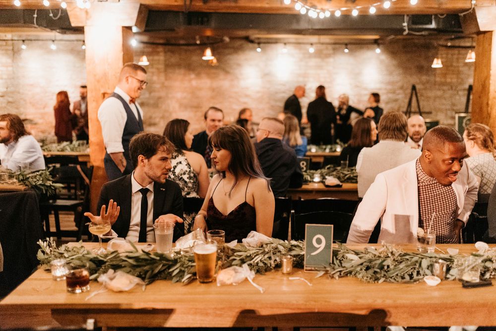 Wedding reception guests laughing at table nine, decorated with lush greenery centerpieces.