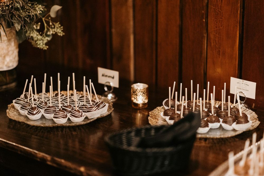 Assorted chocolate-dipped cake pops arranged on platters on a rustic wooden dessert table.