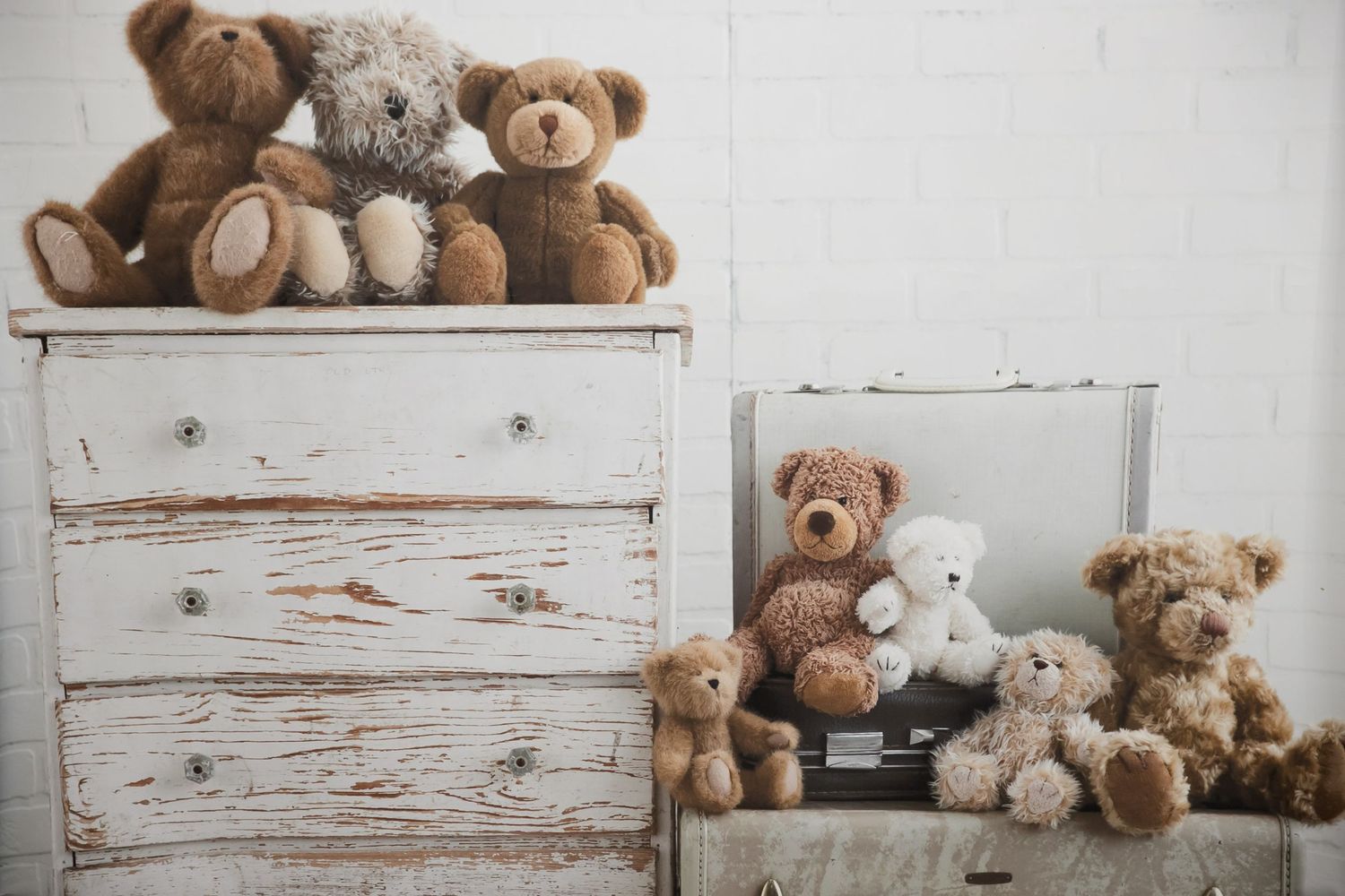 Collection of teddy bears arranged on distressed white wooden furniture creates a charming vintage display.