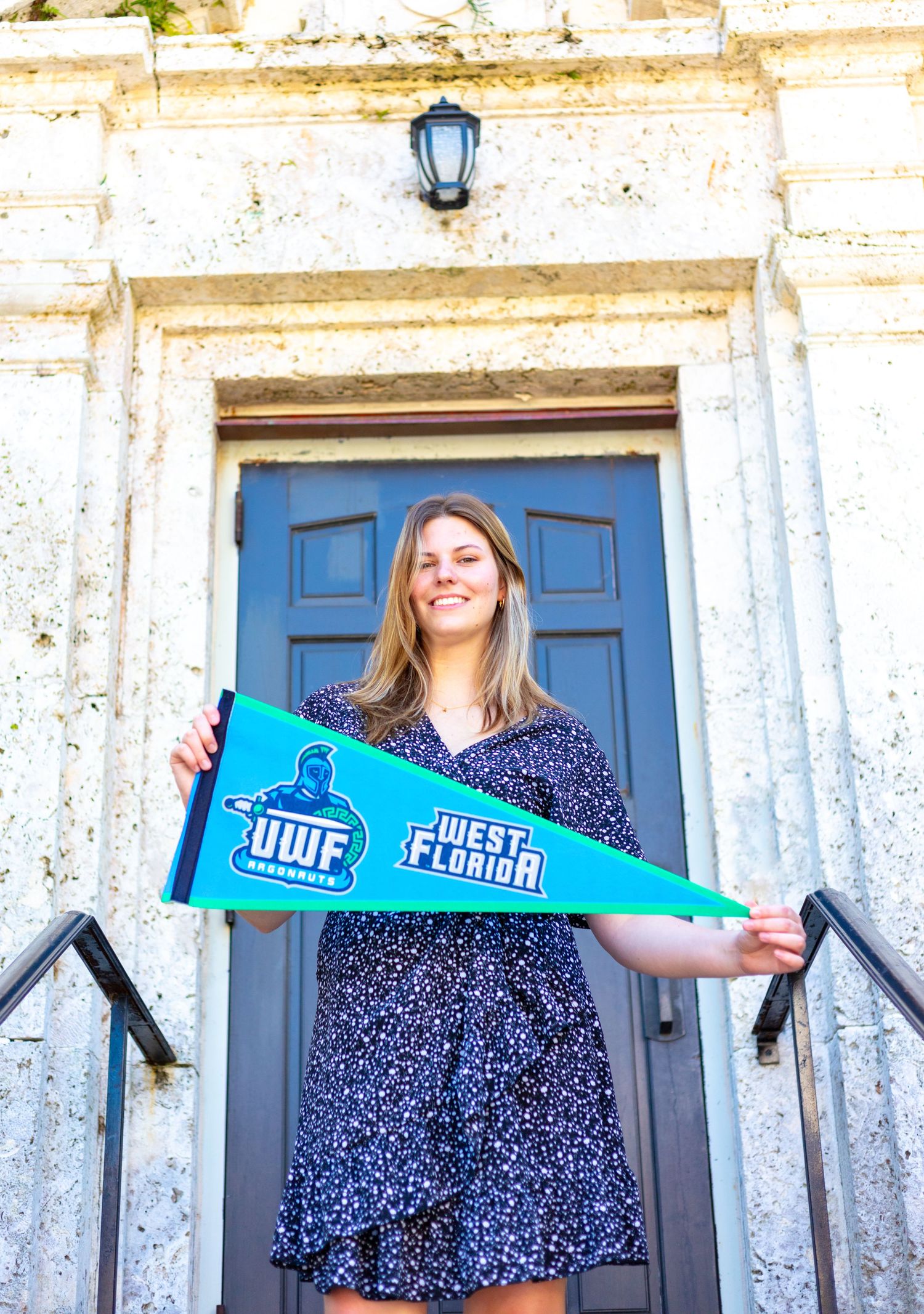 Graduate holding a blue university pennant in front of a historic blue door. Rollins College, Florida