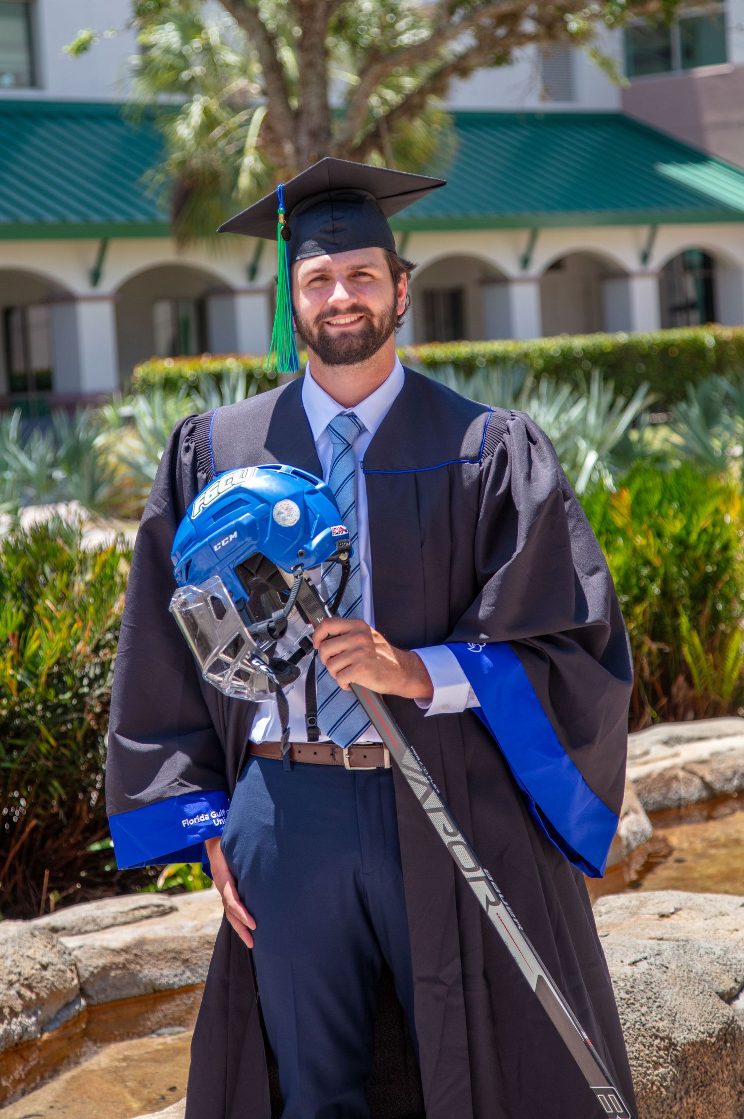 Graduate in cap and gown holds decorated graduation cap in front of campus garden. Florida Gulf Coast University, Florida