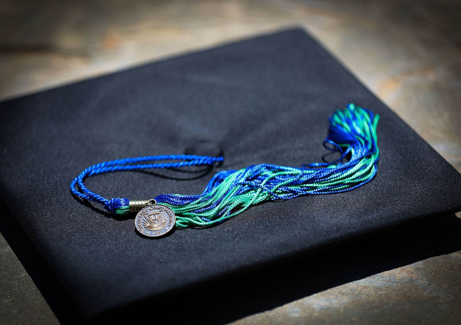 Blue and turquoise graduation tassel resting on black graduation cap. Florida Gulf Coast University, Florida