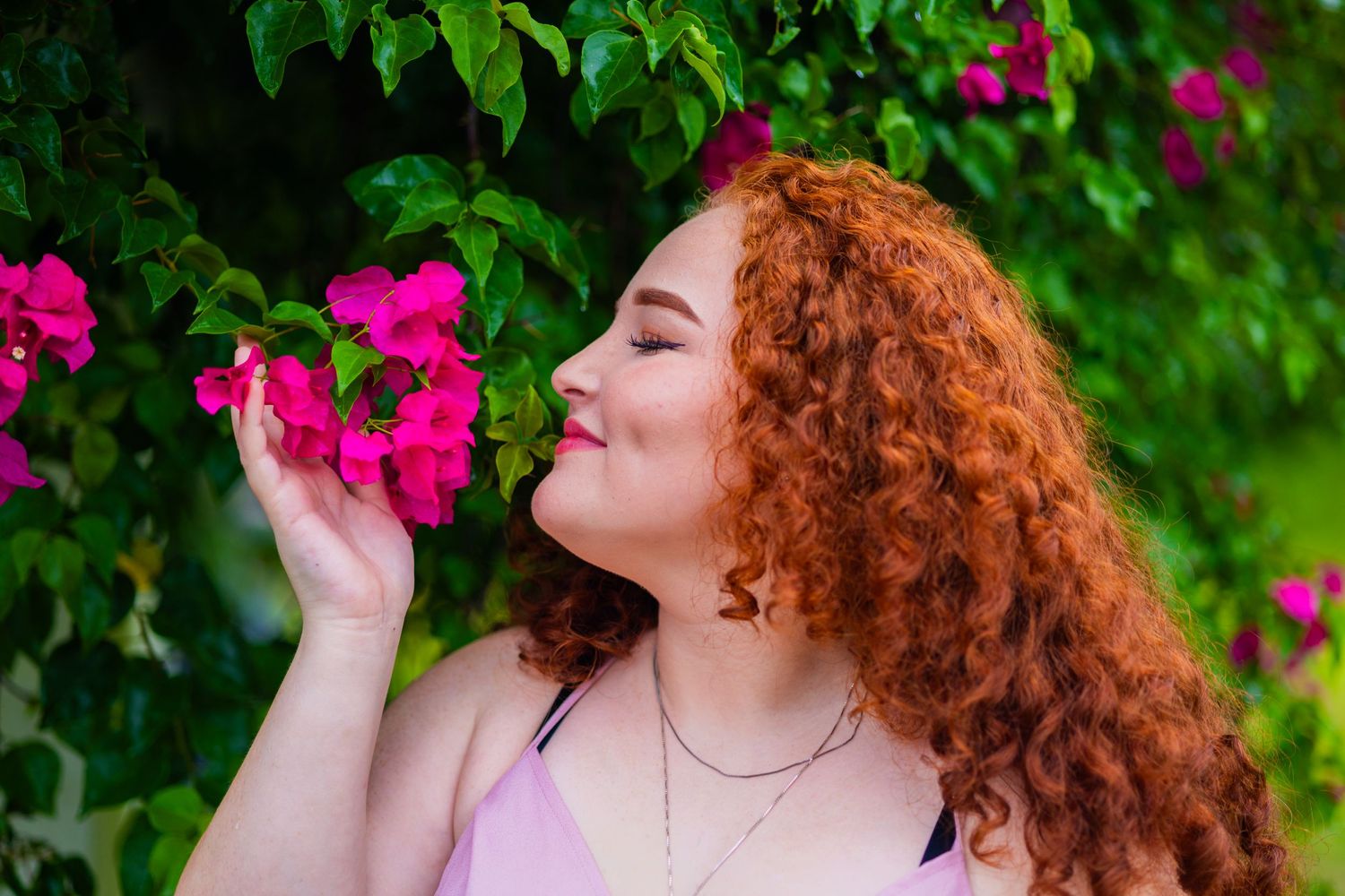 Person with curly red hair smelling bright pink flowers in garden setting. Geneva, Florida
