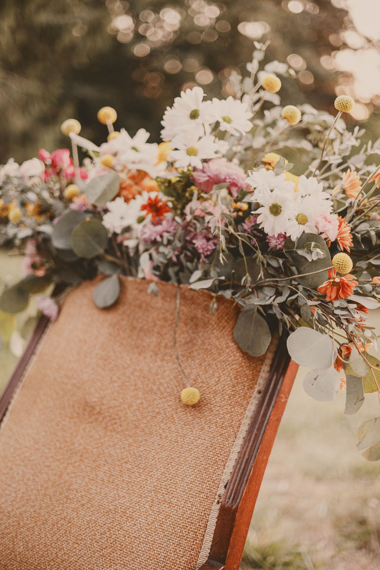 Close-up of rustic floral arrangement with daisies and eucalyptus on brown surface.