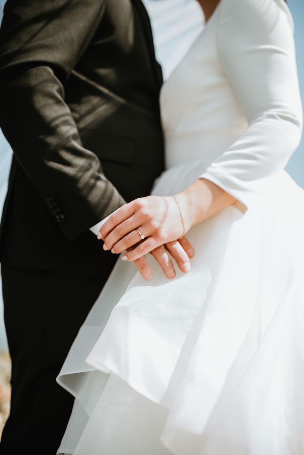 Close-up of newlyweds holding hands, showing contrast between black suit and white wedding dress.