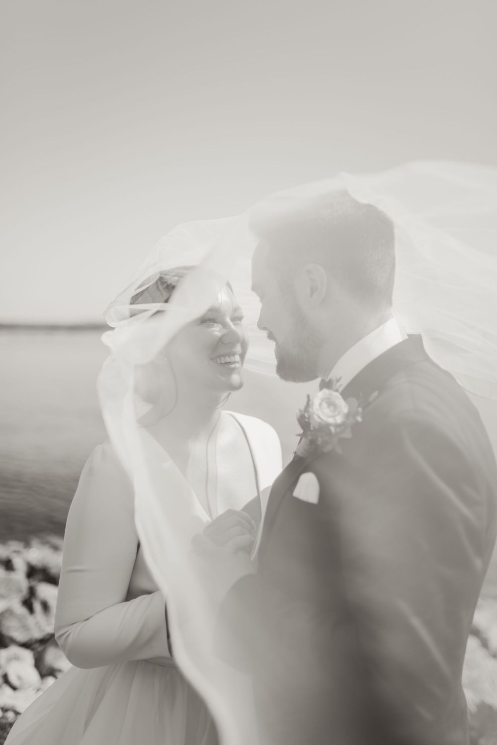 Black and white seaside wedding portrait with bride's veil flowing in the breeze.