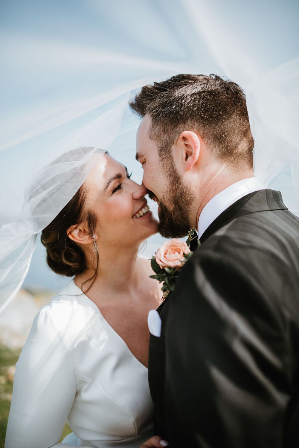 Intimate wedding portrait capturing a tender moment between newlyweds against a blue sky.