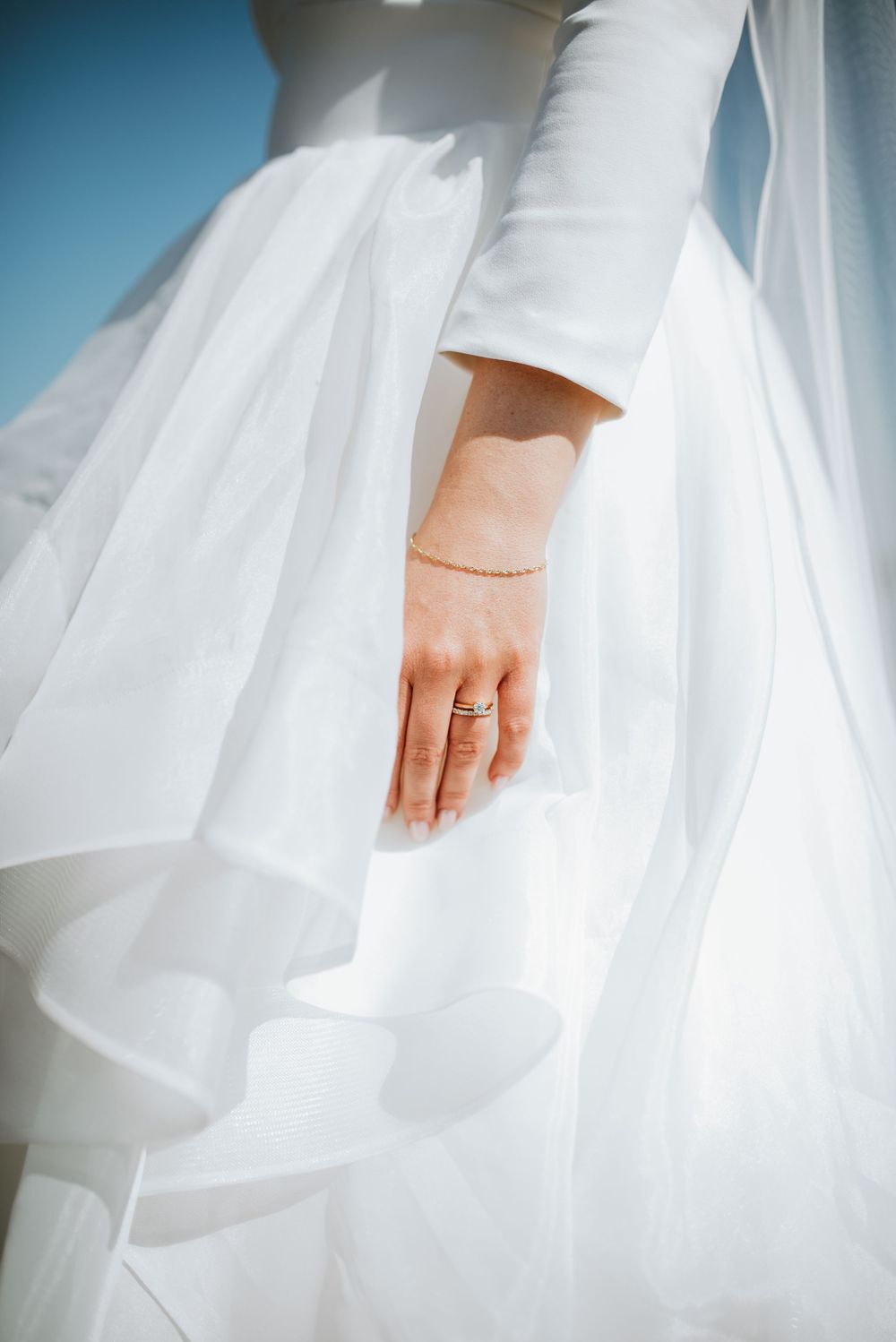 Close-up of a bride's hand with wedding ring against flowing white dress fabric.