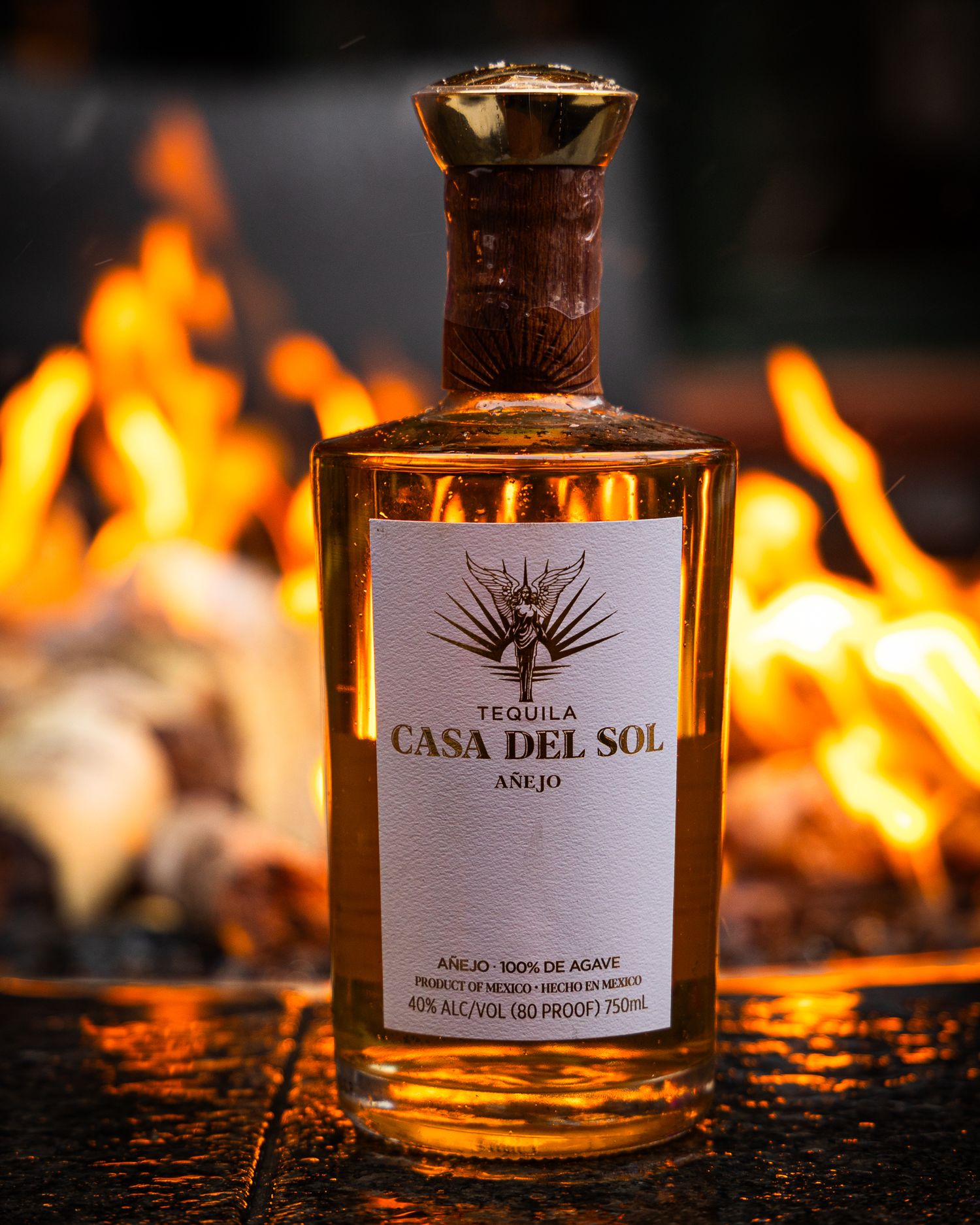 A bottle of Casa Del Sol tequila illuminated by warm firelight with flames glowing in the background.