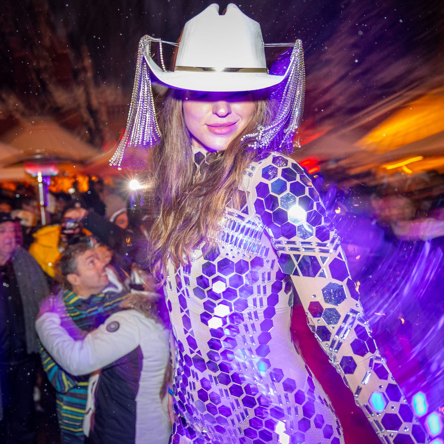 A festival goer in a white cowboy hat and illuminated purple LED outfit dances at a nighttime event.