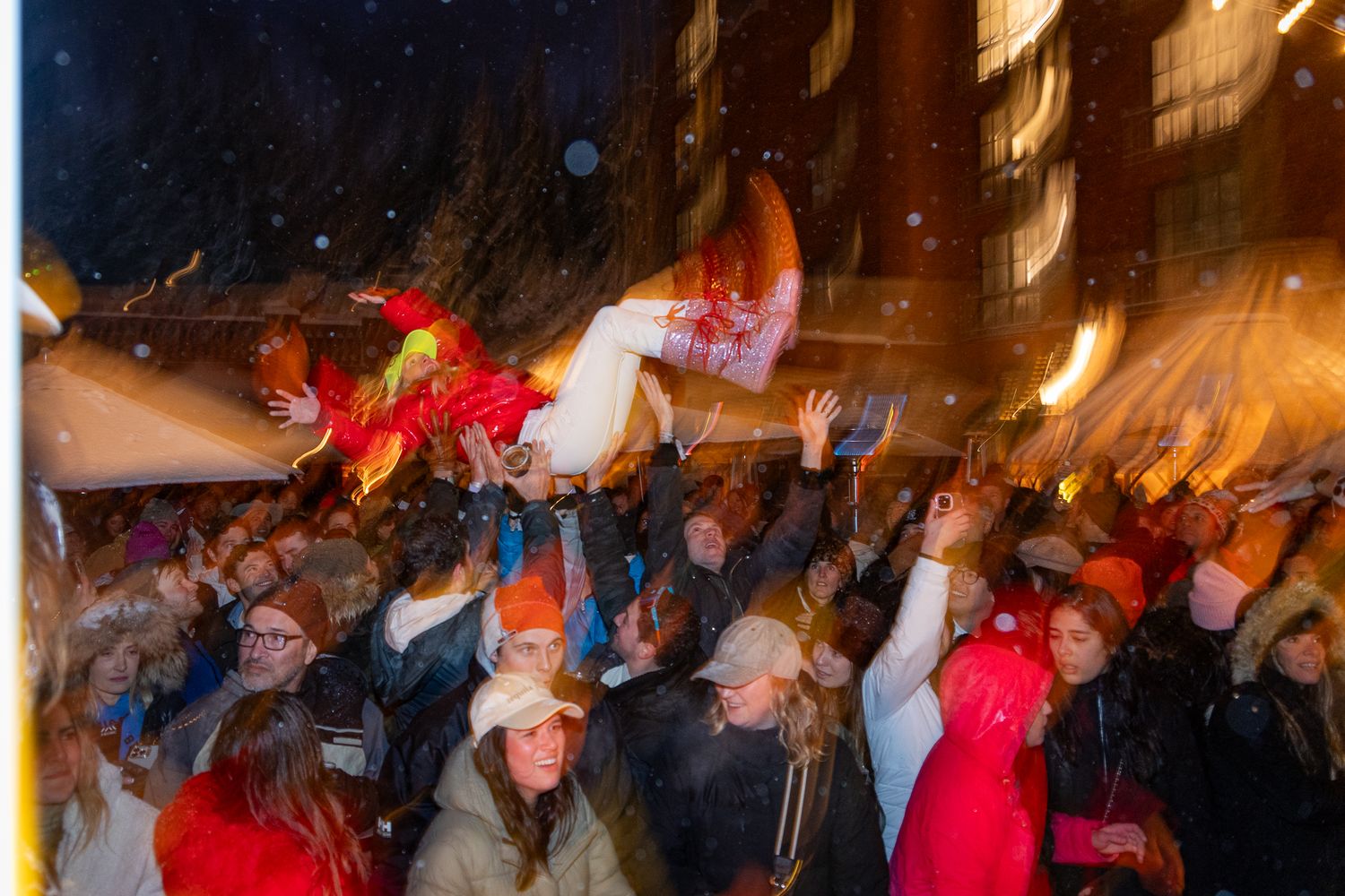 A crowded outdoor celebration at night with blurred motion of people waving colorful flags and lights in winter weather.