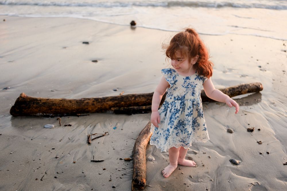 Punta Mita family photographer captures a child in a floral dress exploring the beach at sunset during a sunset family photo session.