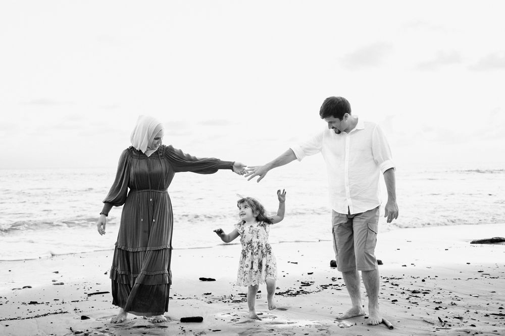Sayulita family photographer captures a family holding hands while walking on a sandy beach during a beach family photo session.
