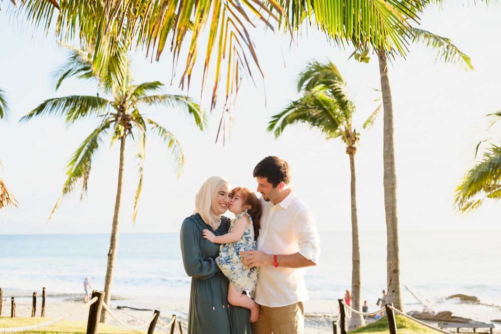Sayulita Family Photographer captures a father, mother, and daughter during a Beach Family Photo Session under tropical palm trees.