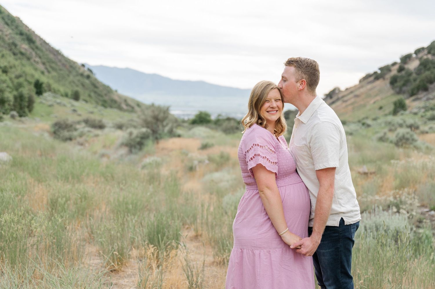 Romantic couple in casual attire standing together in a mountain valley landscape.