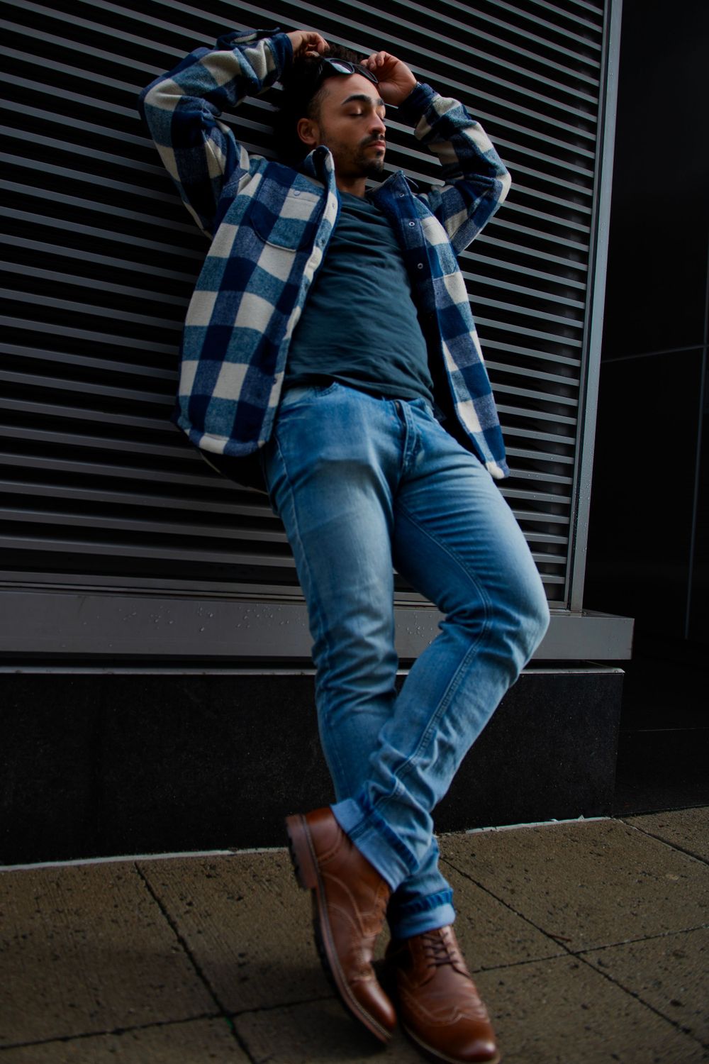 Street style photo of person in blue plaid jacket and jeans against modern architecture.
