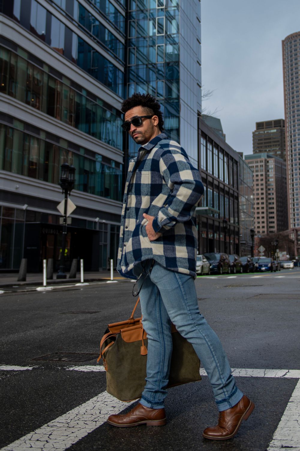 Urban fashion shot with plaid jacket and leather bag crossing city street.