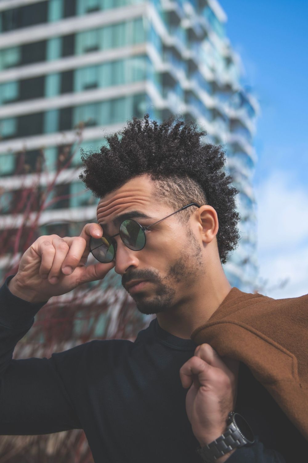 Close-up portrait with sunglasses against modern architecture and blue sky background.