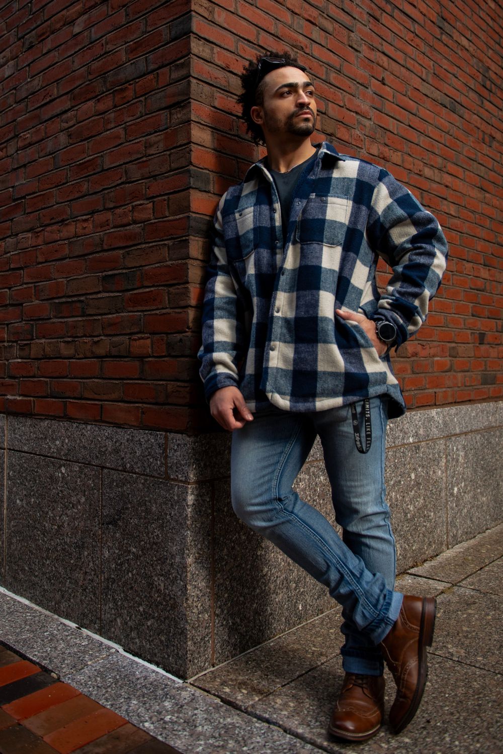 Street style portrait against brick wall featuring plaid jacket and casual denim.